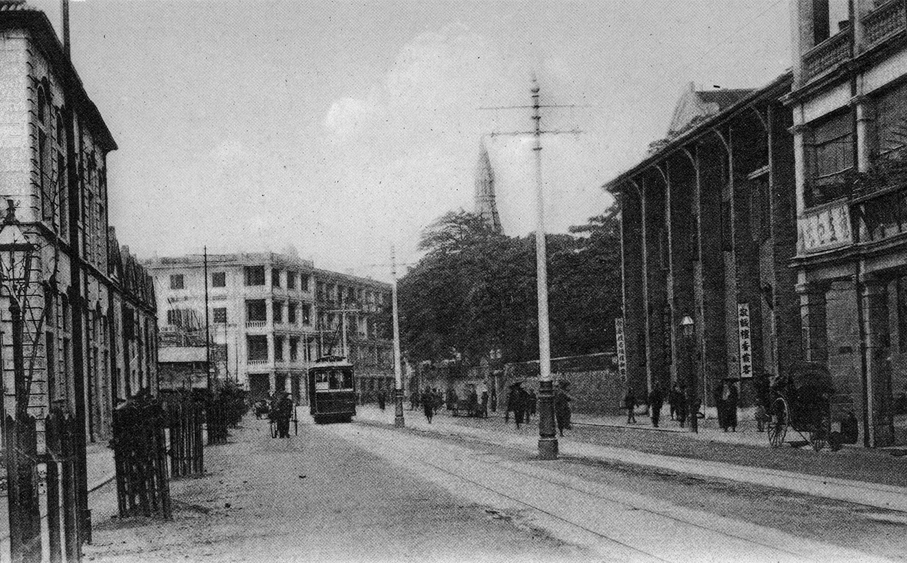 約1910年的德朝道西。電車剛好停在西邊街站，其左為興建中的均益貨倉（現均益大廈），右邊有尖塔的建築物則是聖彼得教堂。（圖片來源：鄭寶鴻提供）